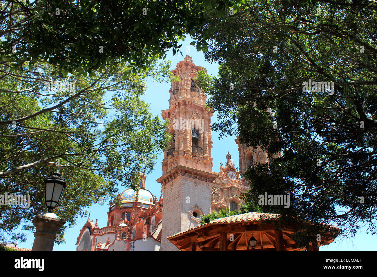 La torre campanaria e piastrellate cupola della chiesa di Santa Prisca visto attraverso gli alberi ombrosi in Plaza Borda, Taxco, Messico Foto Stock