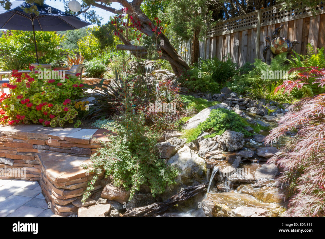 Funzione di acqua corrente con vegetazione lussureggiante in un bellissimo cortile impilati con parete in lastricato Foto Stock