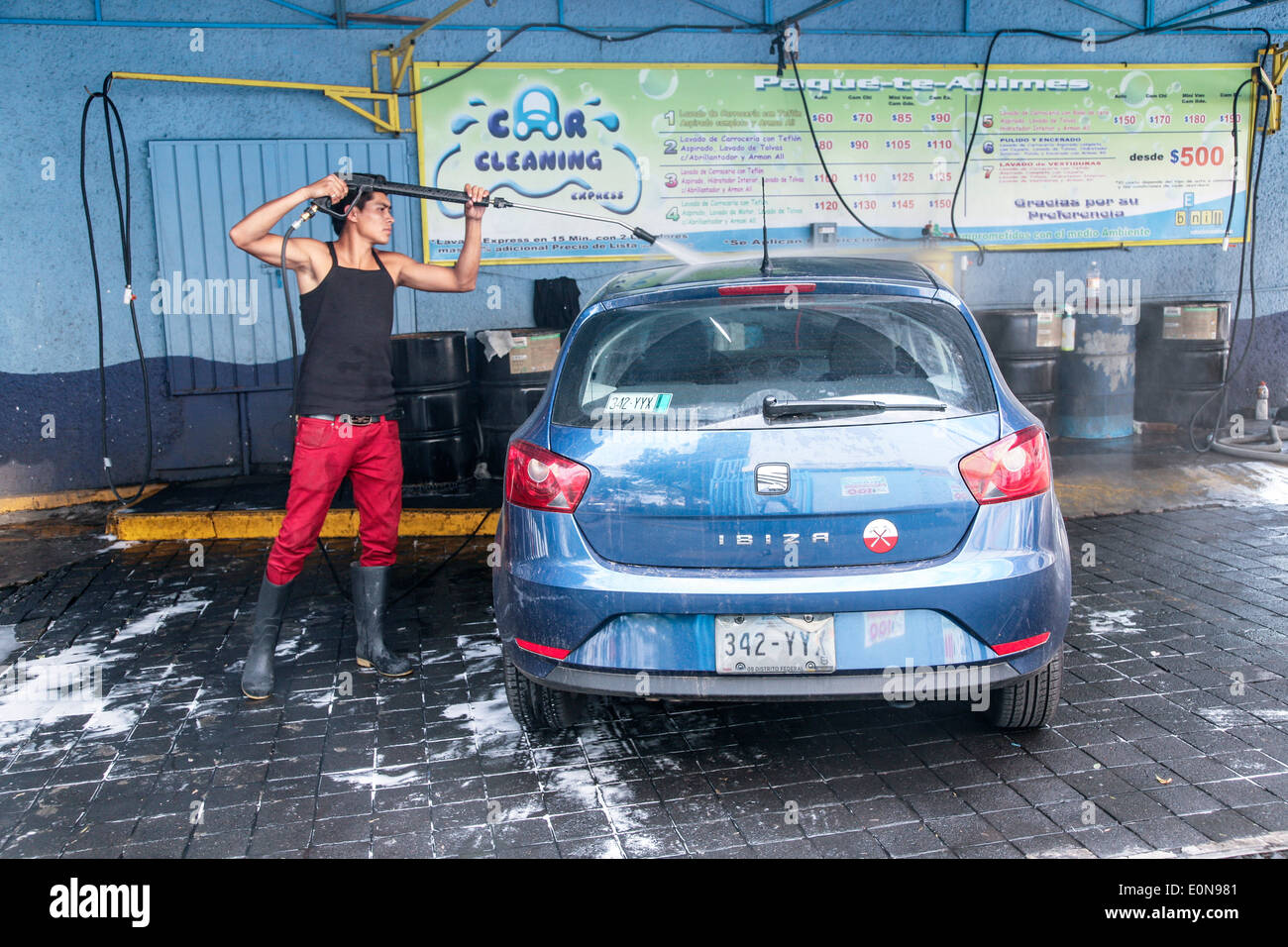 Giovane uomo messicano si muove come un ballerino come egli lava un brillante blu berlina Ibiza auto di lusso a mano a Città del Messico per il lavaggio di auto Foto Stock