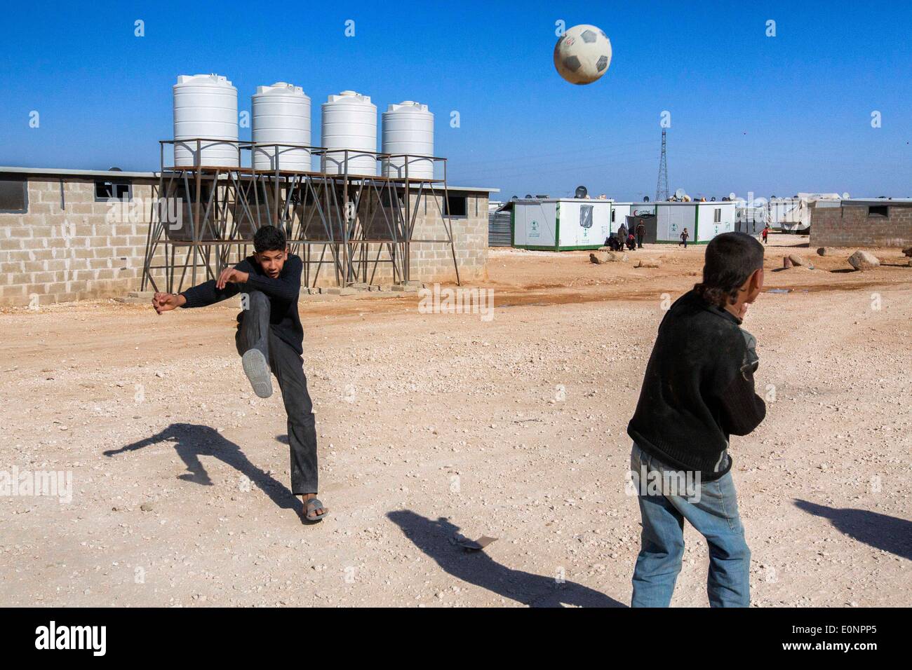 Zaatari Camp, Al Mafraq, Giordania. 8 Feb 2014. I rifugiati di Zaatari - di una partita di calcio o futbol, è un regolare vista all'interno del camp. Dietro i giocatori è una delle decine di ripiego servizi igienici con serbatoi di acqua che la somministrazione di camp deve riempire regolarmente per installatori. Nel deserto giordano, 10 chilometri dalla frontiera siriana si trova un campo profughi noto come Zaatari. Essa è la casa per oltre 110.000 sfollati fuggiti dalla guerra in Siria dal luglio 2012. La maggior parte di questi rifugiati sono dalla regione meridionale di Daraa dove i combattimenti sono tra i peggiori visto in il siriano C Foto Stock