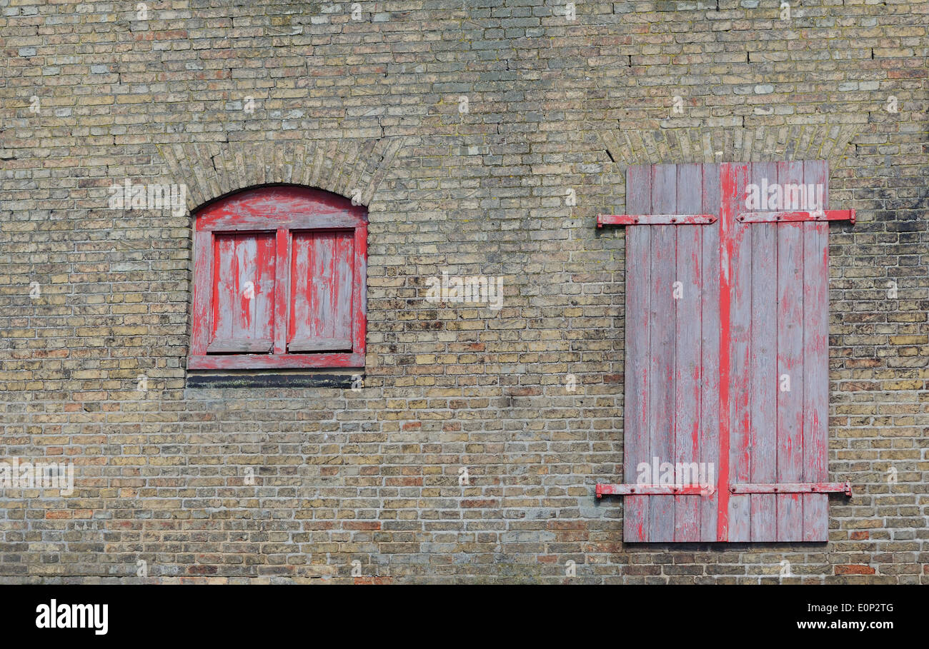 Sbiadita dipinte di rosso porta e finestra in un muro di un magazzino. King's Lynn, Norfolk. Regno Unito. Foto Stock