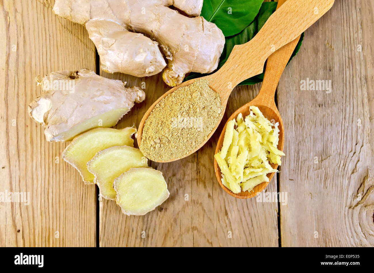 Grattugiato e lo zenzero in polvere in due cucchiai di legno, radice di zenzero, foglie verdi sul pannello di legno Foto Stock