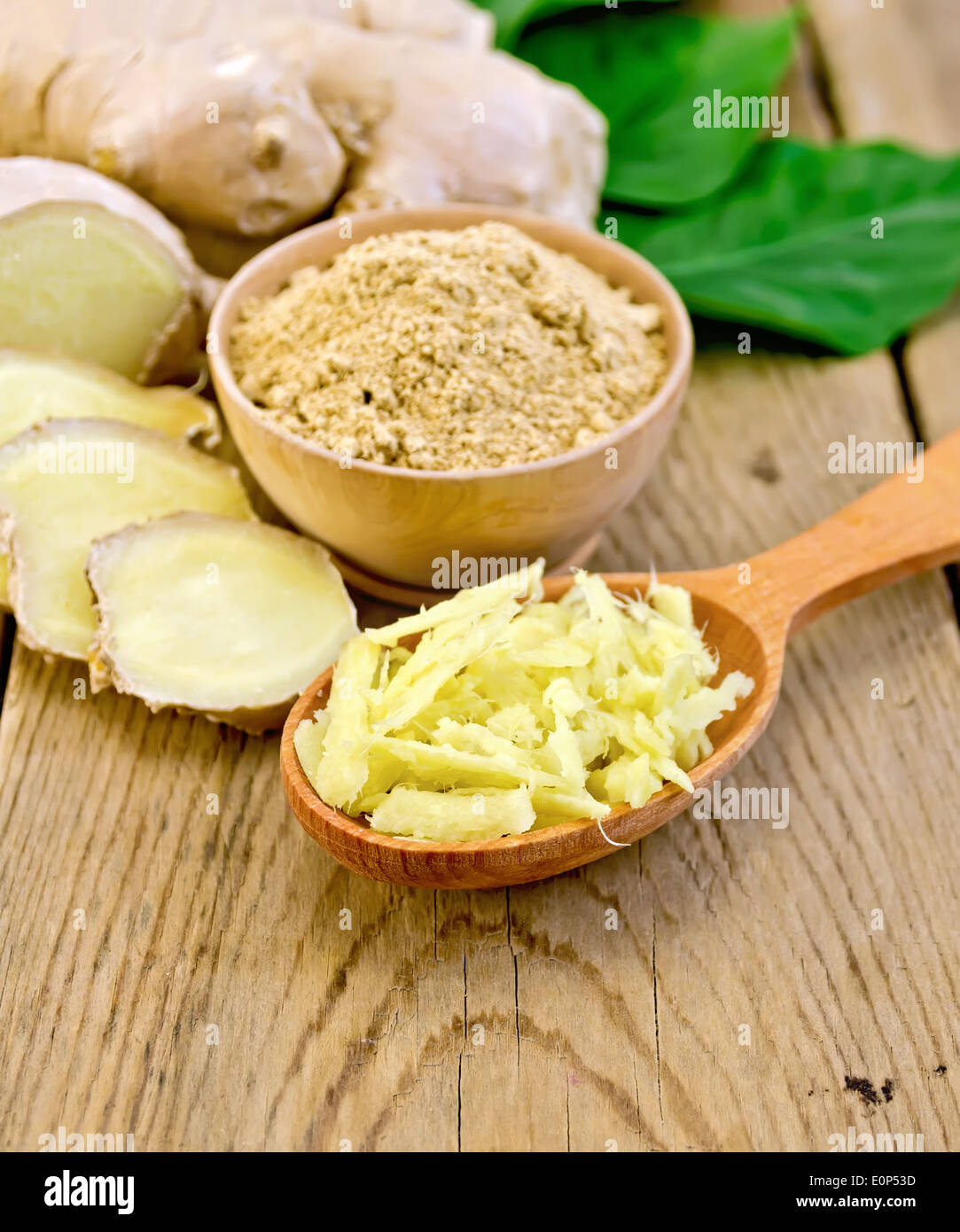 Lo zenzero in polvere in un recipiente, il cucchiaio di legno con lo zenzero grattugiato, radice di zenzero, foglie verdi sullo sfondo delle tavole di legno Foto Stock