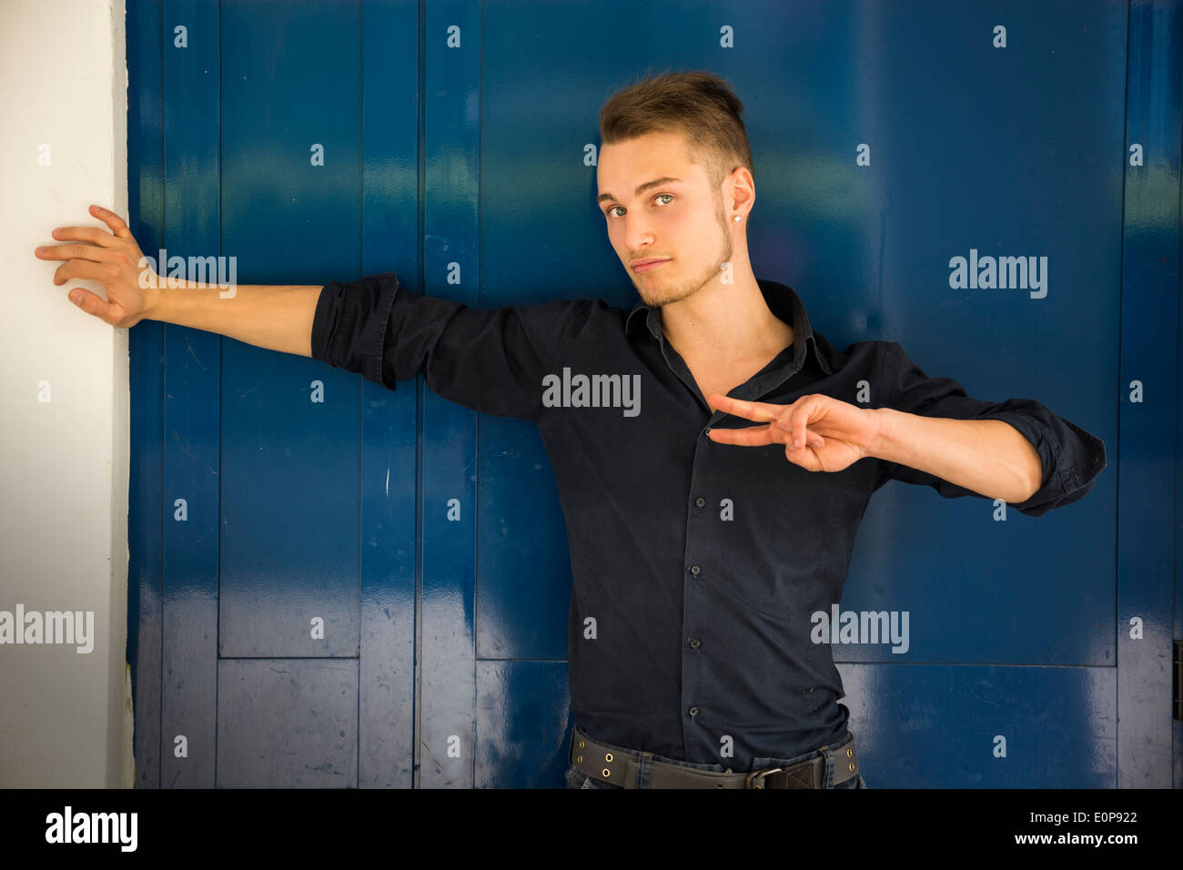 Attraente bionda e giovane uomo contro blu porta di metallo facendo segno di pace con le dita Foto Stock
