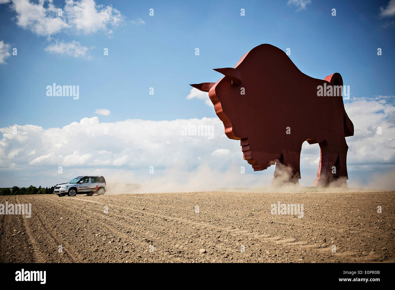 Un SUV con i giornalisti scorre attraverso un campo per visualizzare una gigantesca statua di bielorusso simbolo nazionale, il Bisonte Europeo, su una autostrada che conduce a Minsk, Bielorussia, Sabato, Maggio 10th, 2014. Le autostrade in Bielorussia non conformi con West norme europee. Western Foto Stock
