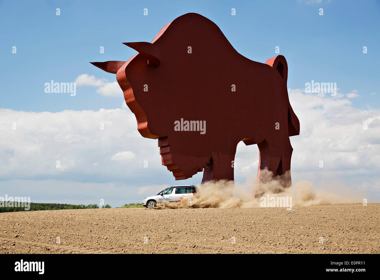 Un SUV con i giornalisti scorre attraverso un campo per visualizzare una gigantesca statua di bielorusso simbolo nazionale, il Bisonte Europeo, su una autostrada che conduce a Minsk, Bielorussia, Sabato, Maggio 10th, 2014. Le autostrade in Bielorussia non conformi con West norme europee. Western Foto Stock