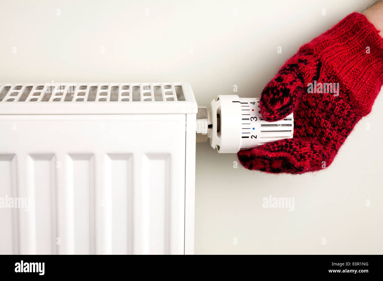 Singola mano umana con maglia guanto ruotando il termostato del radiatore Foto Stock