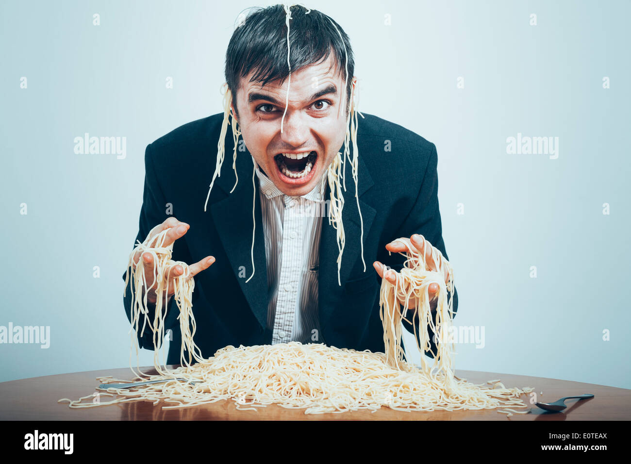 Crazy consumismo concetto. Mad nasty imprenditore mangiare pasta sul tavolo. Foto Stock
