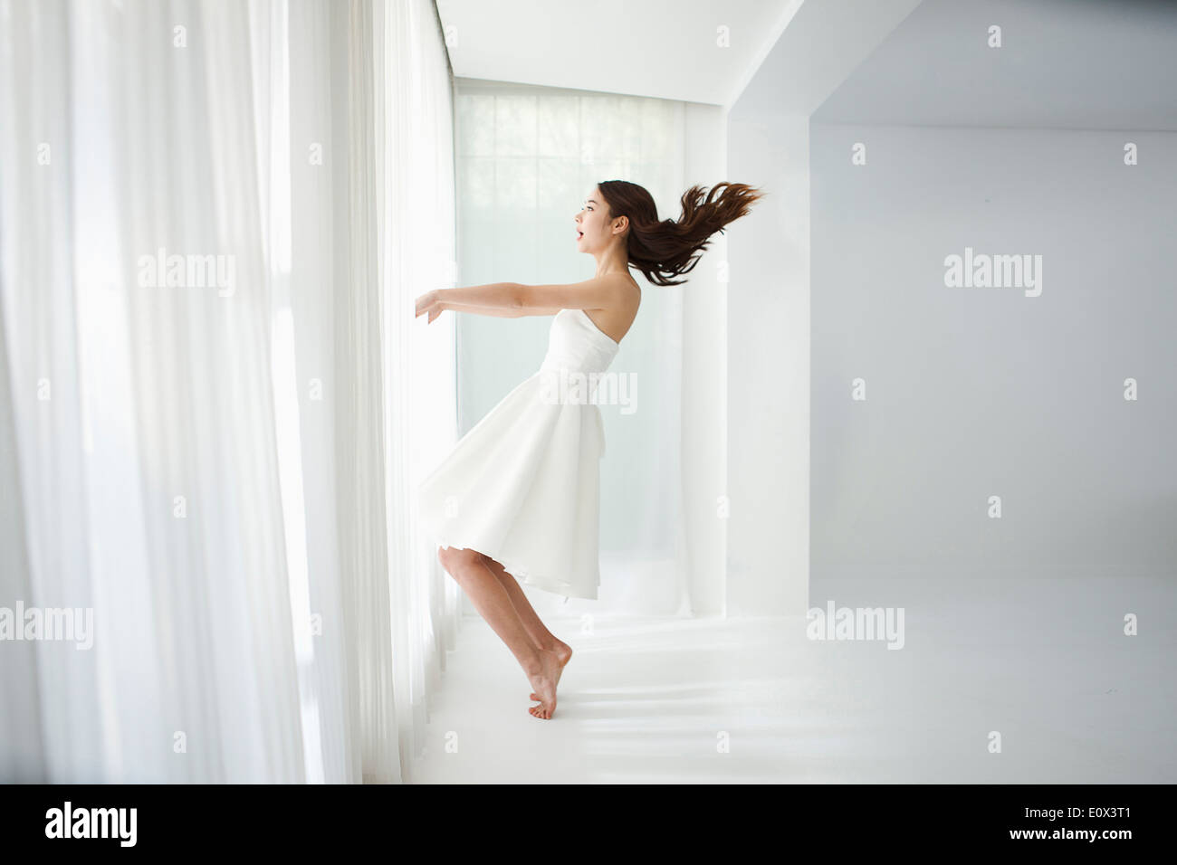 Una donna l'apertura di una finestra di una camera bianca Foto Stock