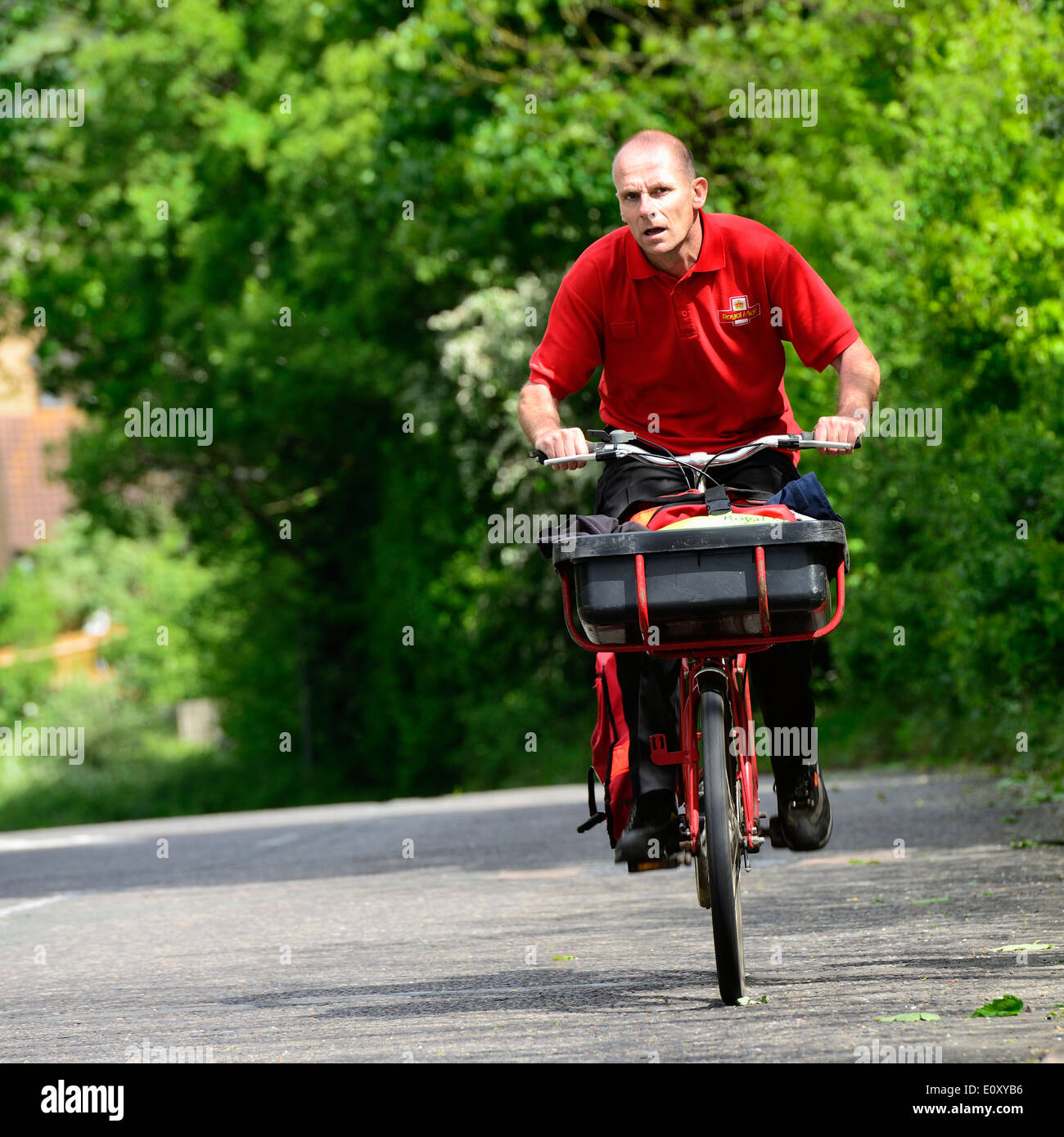 Royal Mail portalettere su una bicicletta con un cestino e bauletto laterale che porta le lettere a cavallo su una ripida collina di Manningtree, Essex, Regno Unito Foto Stock