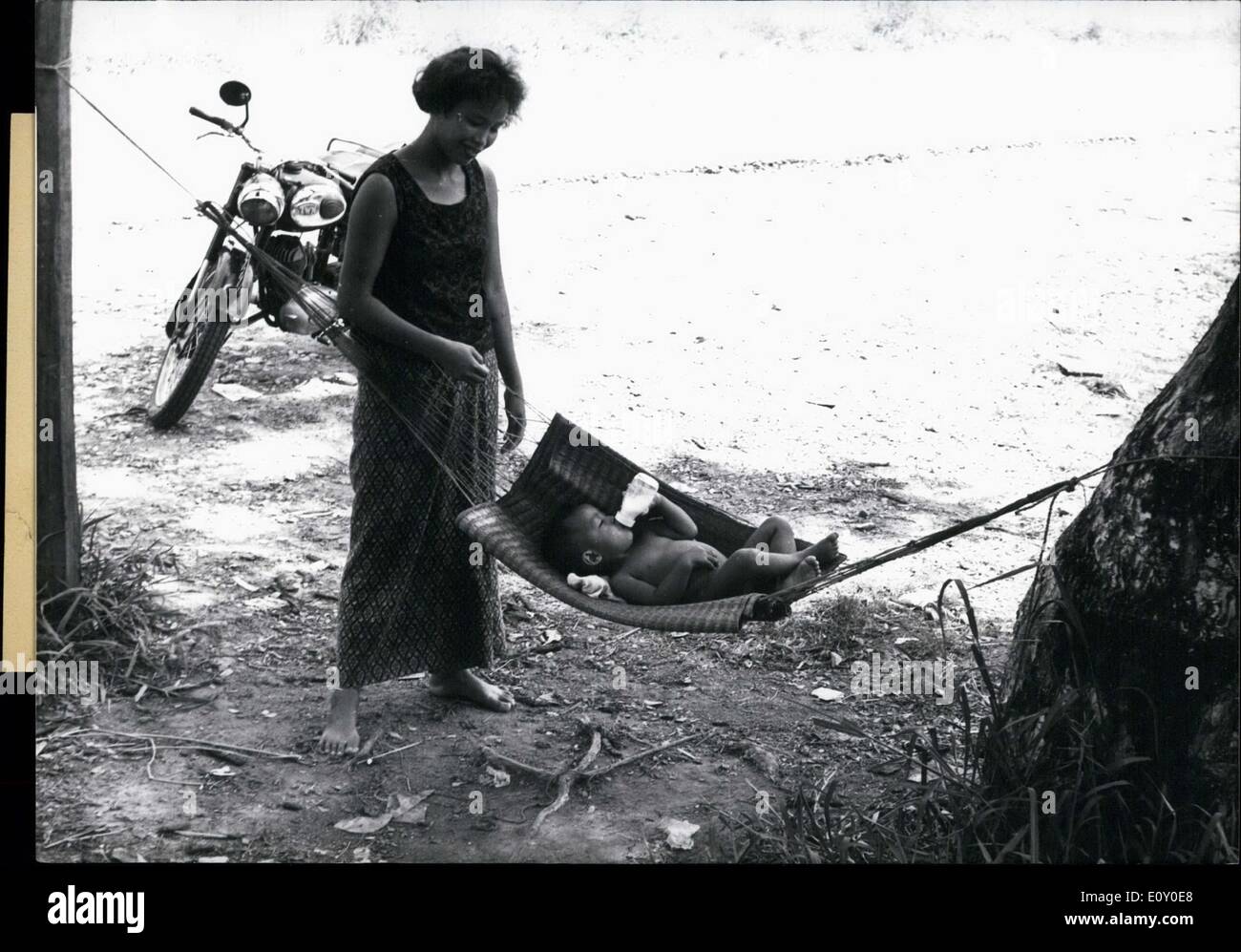 Maggio 04, 1968 - Questa Thailandia infilate madre una culla fino tra alberi e collocato il suo bambino in esso. La culla è sotto l'ombra di una partita di alberi e proteggere il bambino dal calore come beve il suo latte. Foto Stock