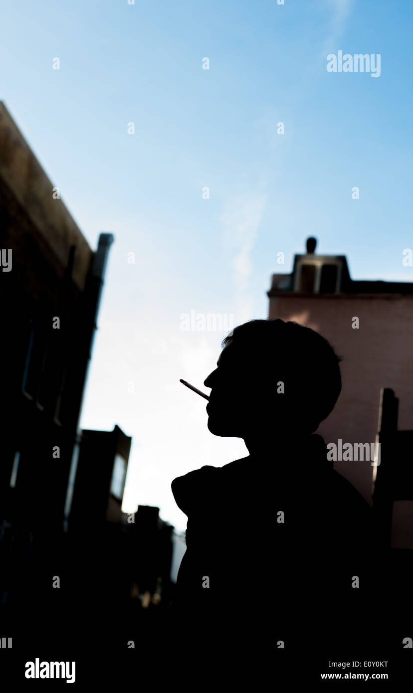 Silhouette di un uomo di fumare contro un cielo blu Foto Stock