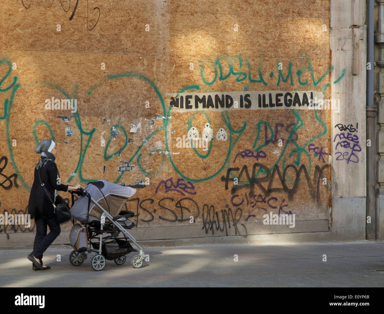 Donna che cammina spingendo la PRAM con graffiti dicendo nessuno è illegale in lingua olandese, Bruxelles, Belgio Foto Stock