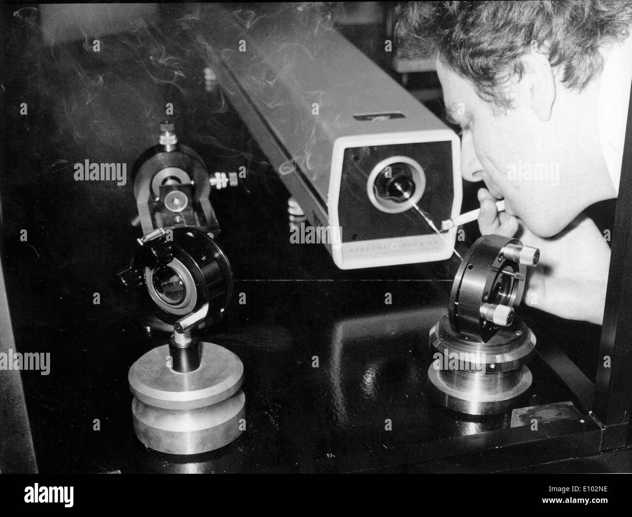 Un uomo un test su un computer che emette un fascio laser di luce soffiando il fumo di sigaretta a fascio per renderlo visibile. Foto Stock
