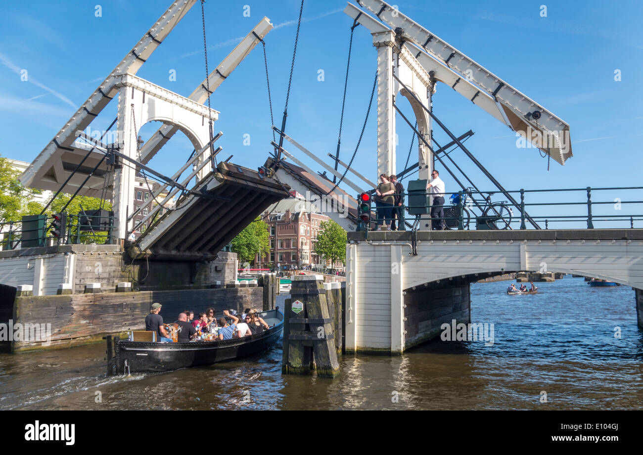 Amsterdam Magere Brug, Skinny Bridge, piccola barca passando ponte levatoio. Un bridgeman sulla bicicletta è la chiusura della parte sollevabile ponte levatoio. Foto Stock