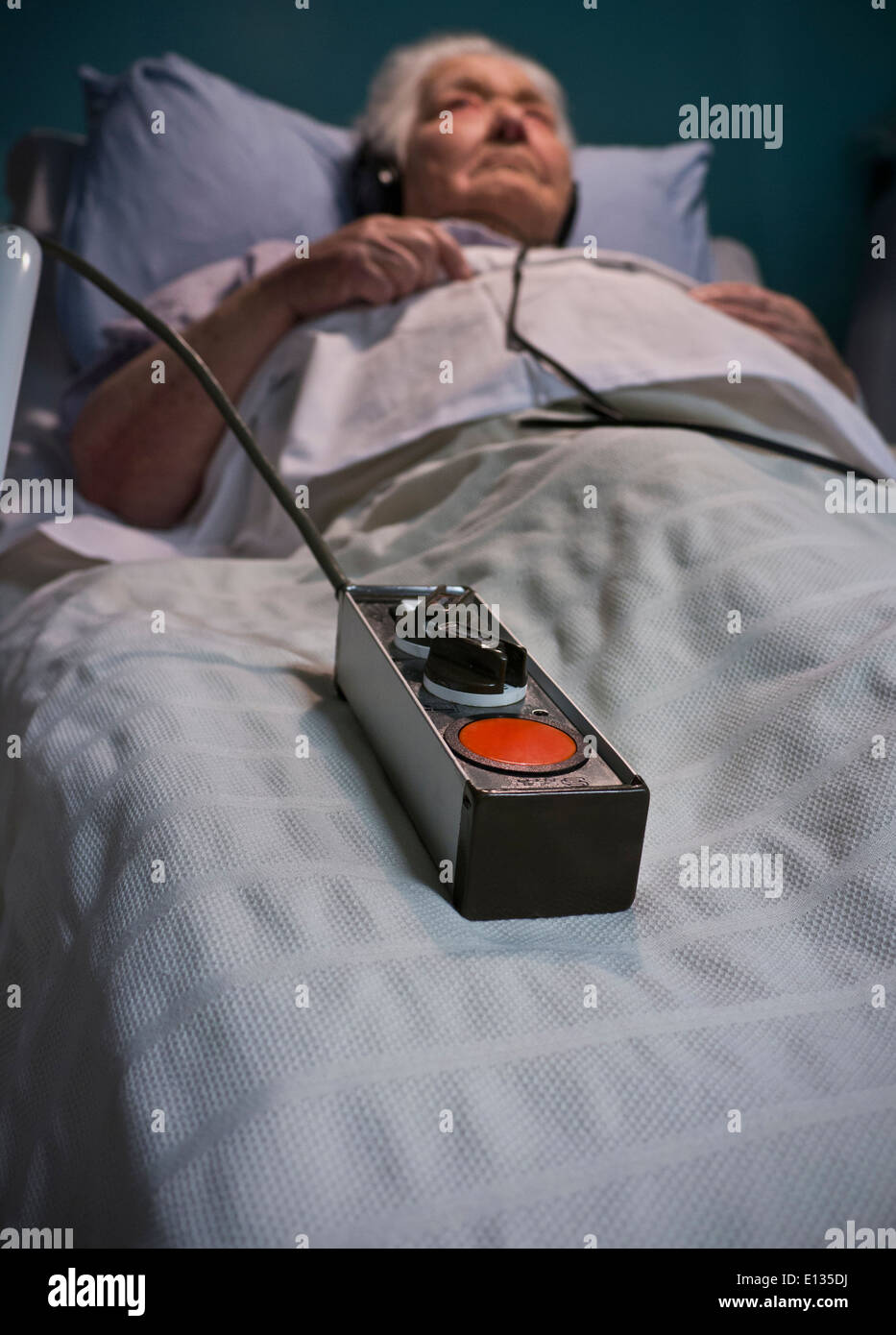 Tastierina CHIAMATE EMERGENZA cura anziana signora che indossano le cuffie in hospital care letto la sera con la chiamata di emergenza Pulsante giacente al suo lato Foto Stock