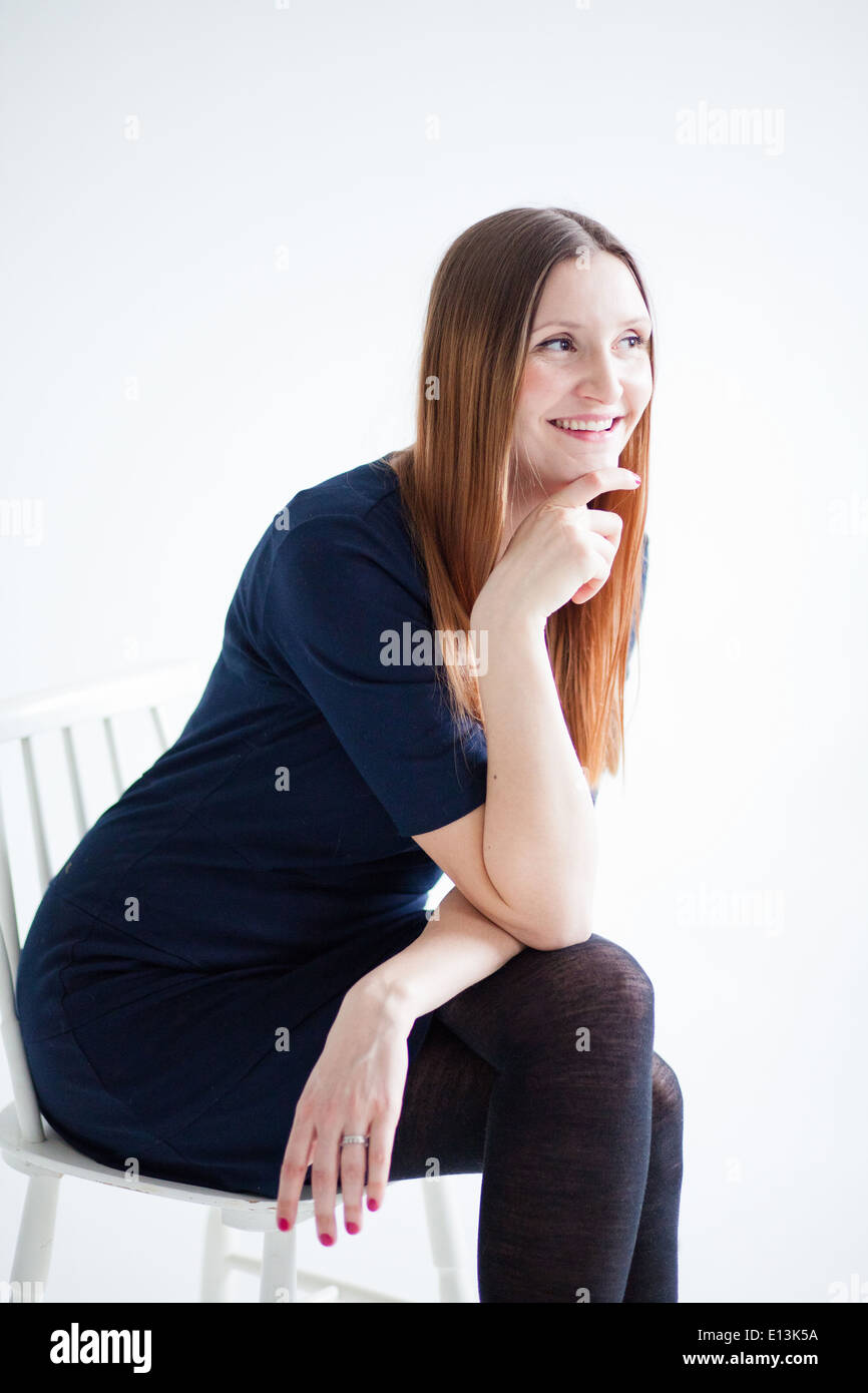 Ritratto in studio di sorridenti donna attraente indossa camicetta blu e seduti in poltrona e tenendo la mano per il mento Foto Stock