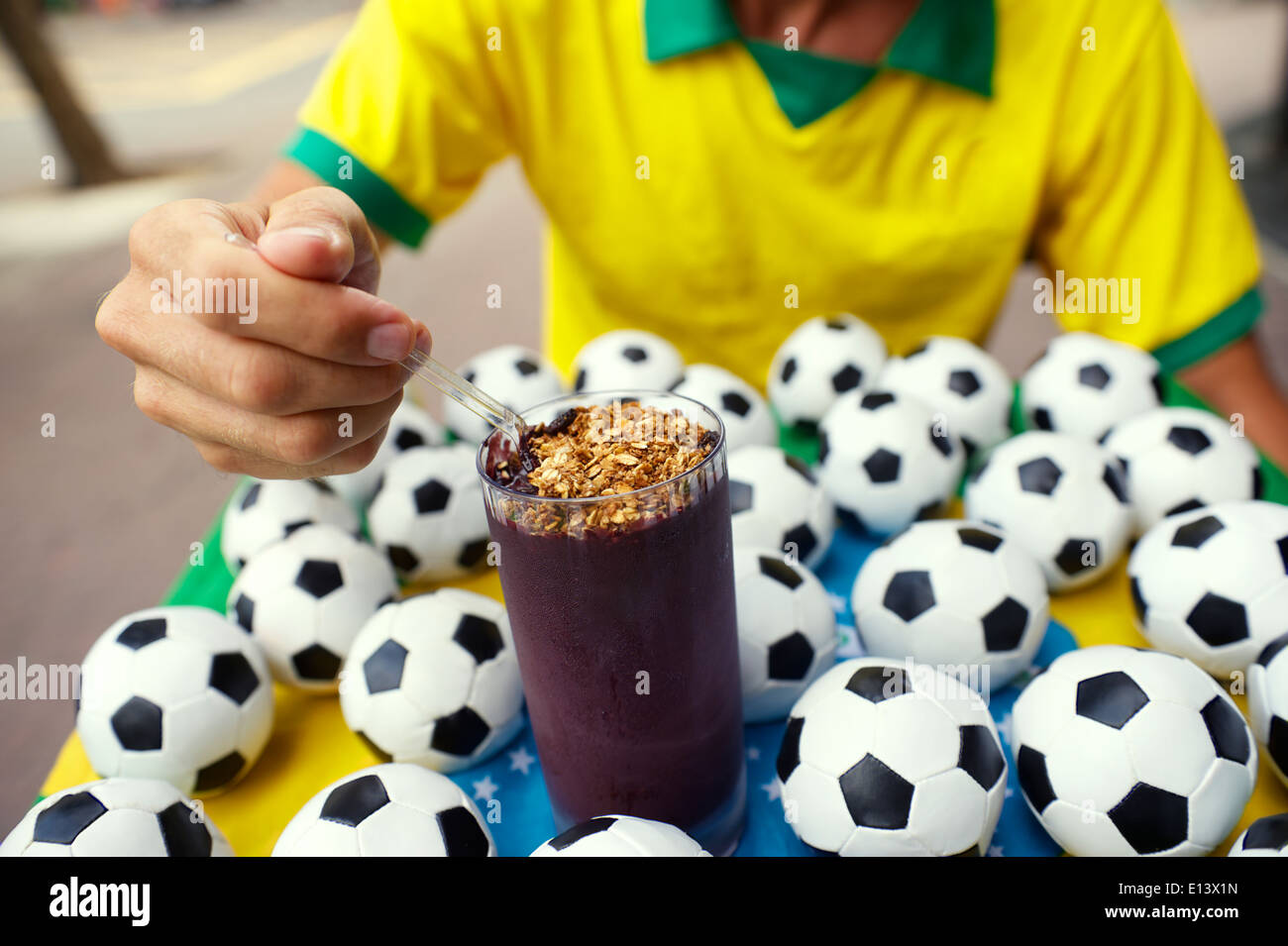 Il calcio brasiliano giocatore seduto a mangiare acai in un vetro circondato da palloni da calcio Foto Stock