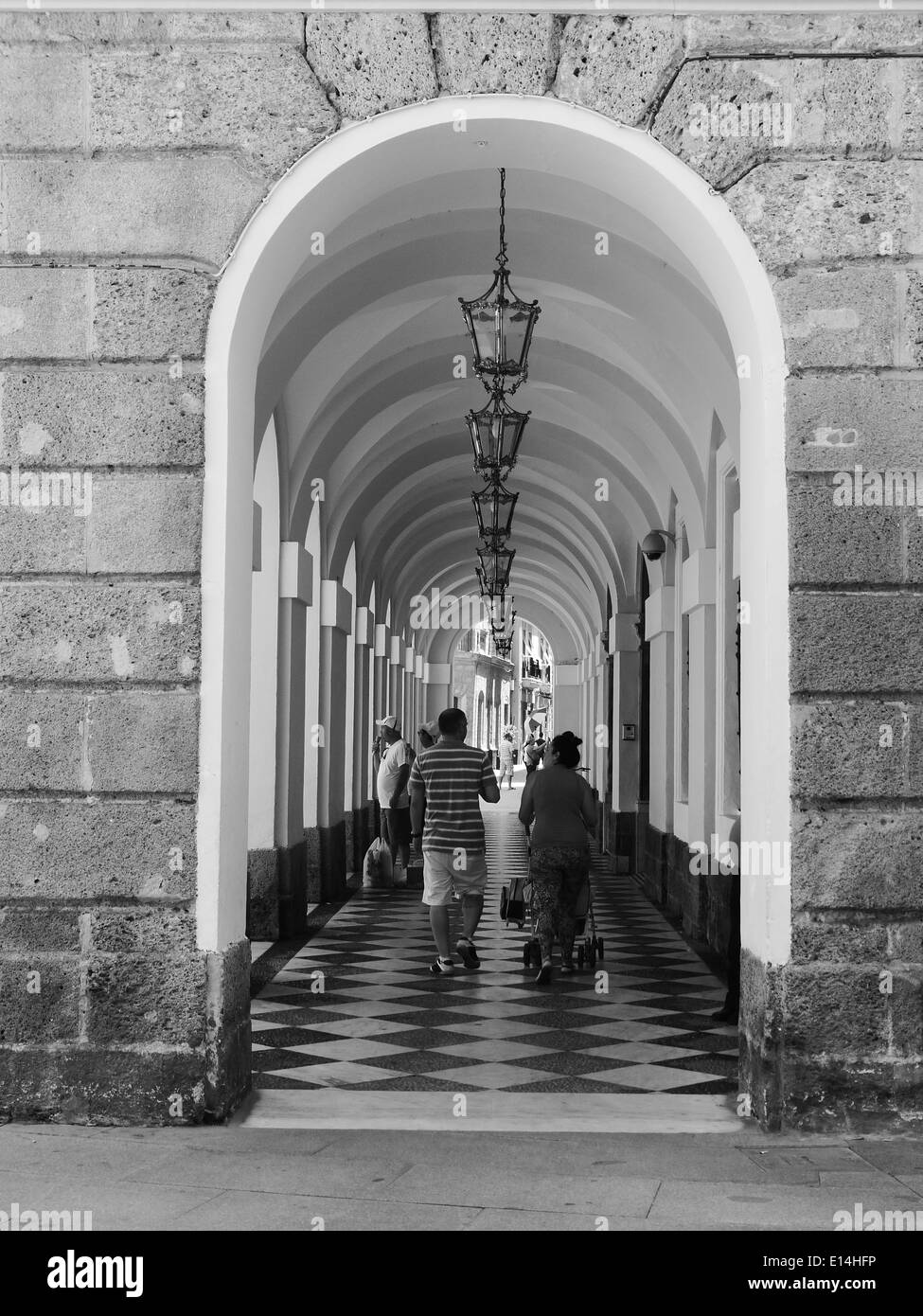 La gente a piedi attraverso una serie di archi a Cadiz, Spagna Foto Stock