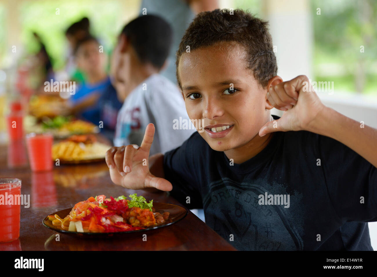 Ragazzo brasiliano nella parte anteriore di una piastra piena di cibo in tavola con altri bambini in un progetto sociale per i bambini di strada Foto Stock