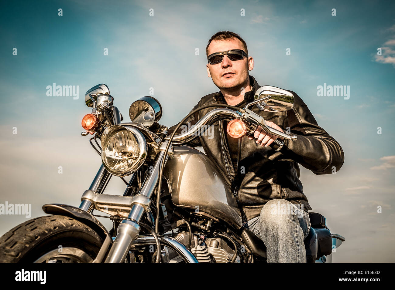 Biker uomo che indossa una giacca di pelle e occhiali da sole seduto sulla sua moto guardando il tramonto. Foto Stock Biker uomo che indossa una giacca di pelle e occhiali da sole seduto sulla sua moto guardando il tramonto. Foto Stock