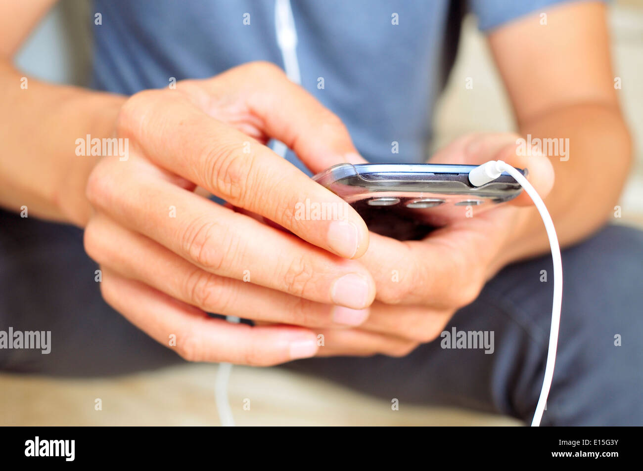 Primo piano di un giovane uomo che ascolta musica o parlando con un auricolare in uno smartphone Foto Stock