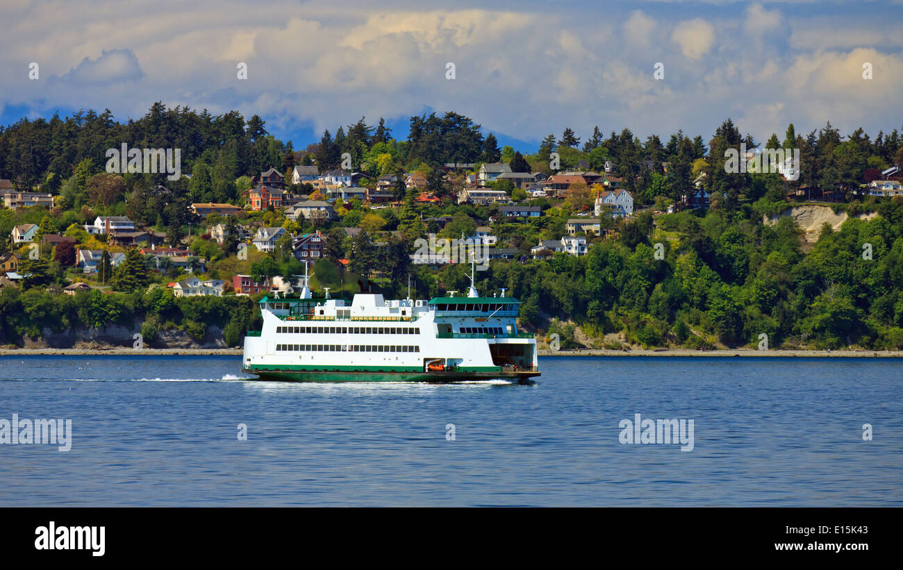 Nave traghetto su acque calme passando da un paesaggio panoramico coperto con alberi verdi e le case sparse lungo il fianco della collina. Foto Stock