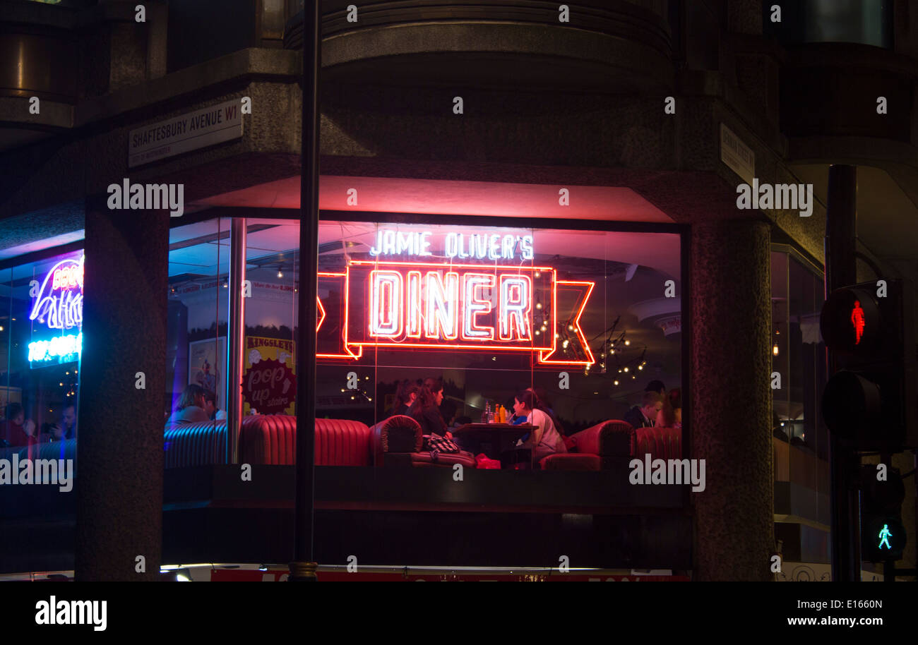 Persone (quattro giovani donne) seduta a tavola nella finestra sotto insegna al neon Jamie Oliver's Diner Shaftesbury Avenue London Inghilterra England Regno Unito Foto Stock