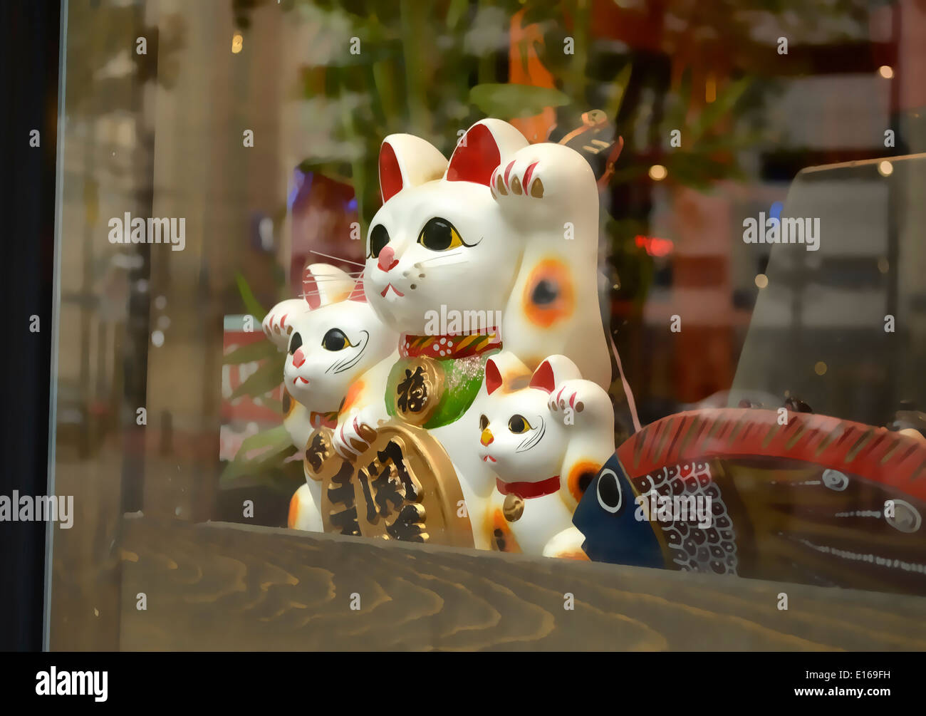 A Maneki Neko giapponese lucky cat statuetta in una vetrina di un negozio con un gatto e due gattini. Foto Stock