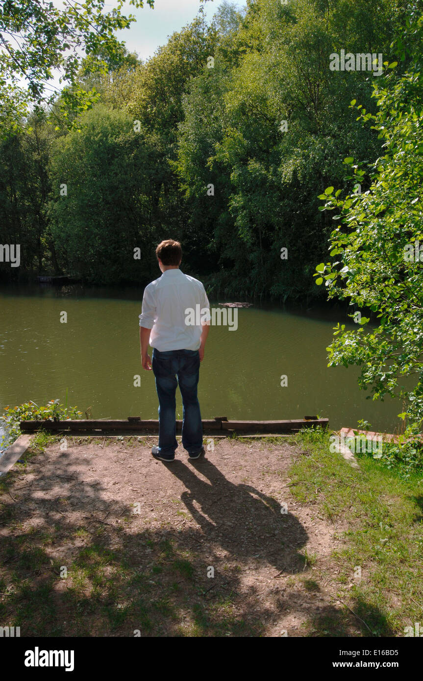 Un uomo adolescente,in piedi sul bordo di un lago di acqua dolce. Foto Stock