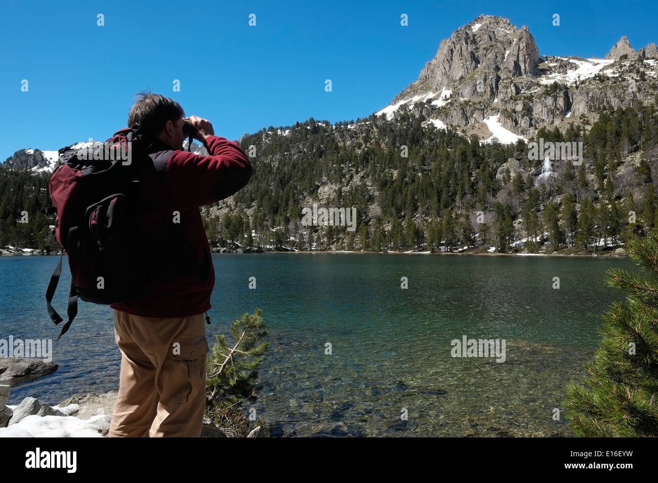 Un escursionista che utilizza binocoli per guardare il lago Estany de la Ratera nel parco Parque Nacional d'aiguestortes i Estany de san Maurici nella valle di Vall De Boi in provincia di Lleida Catalogna Spagna Foto Stock
