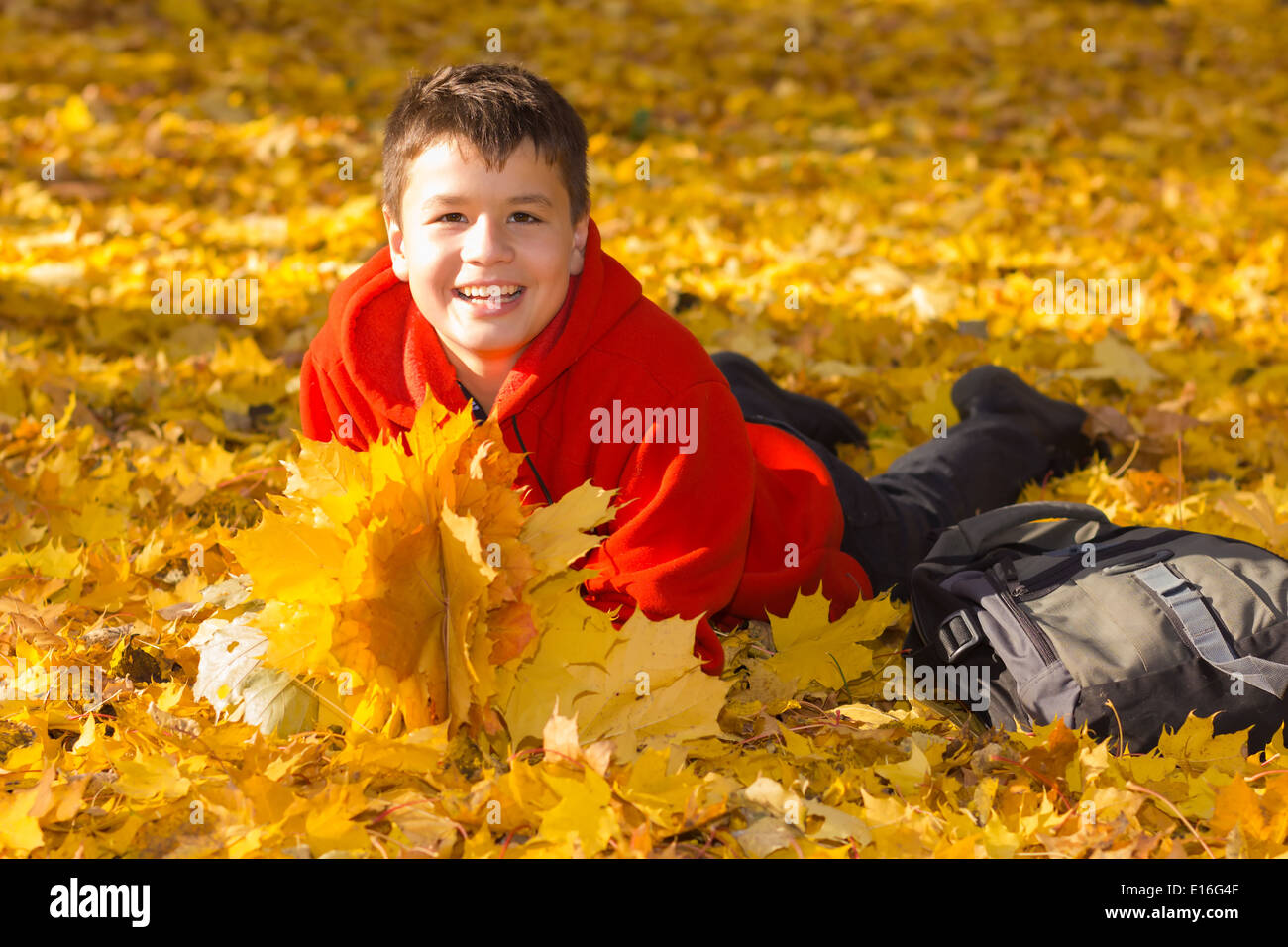 Sorridenti caucasian boy con autunno foglie di acero giacente in una giornata di sole nel parco Foto Stock