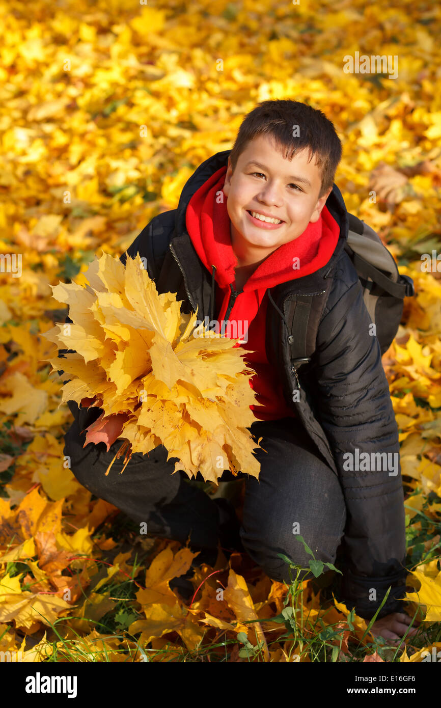 Sorridenti caucasian boy con autunno foglie di acero in una giornata di sole nel parco Foto Stock