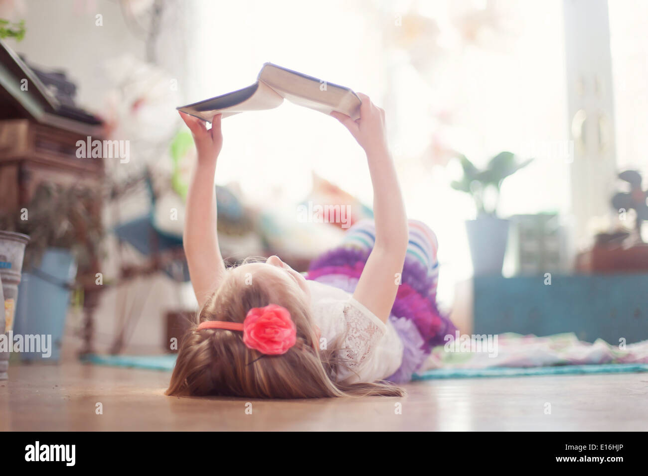 La ragazza (4-5) giacente sul retro del libro di lettura a casa Foto Stock