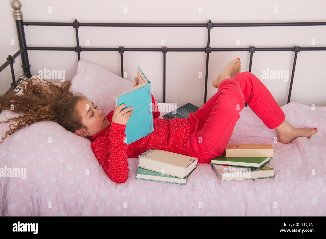 La ragazza (10-12) la lettura di un libro sul letto, Milano, Italia Foto Stock
