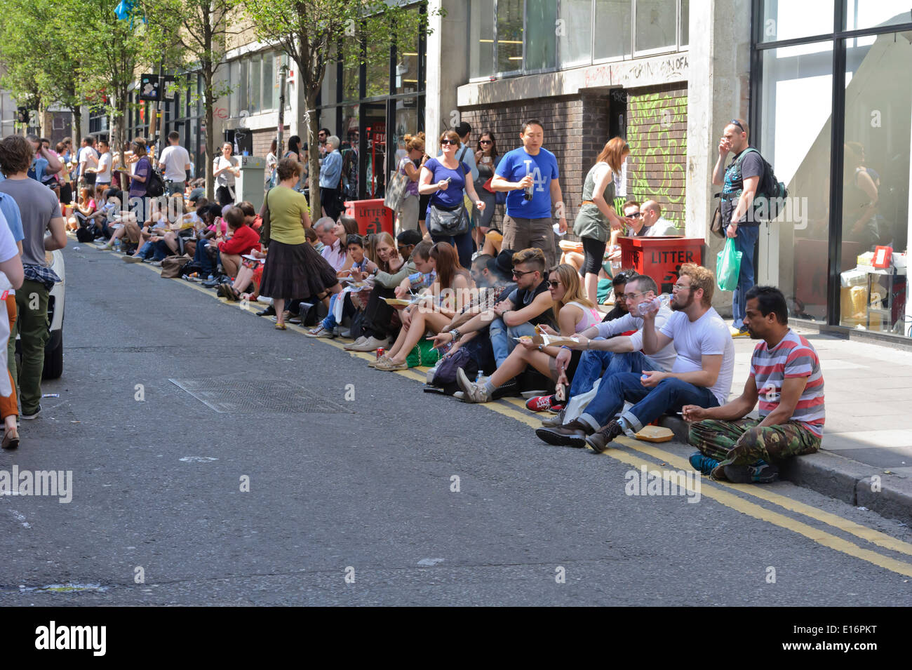Persone che fanno il miglior del clima britannico di seduta sul marciapiede e mangiare cibo piccante acquistato da ristoranti di cucina asiatica. Foto Stock