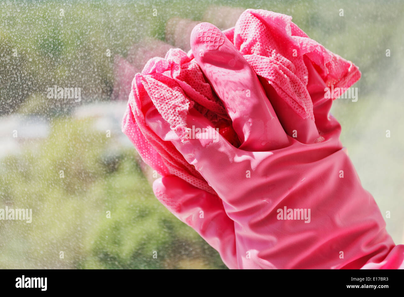 La mano in rosa guanto di gomma lavaggio vetro della finestra mediante un panno umido Foto Stock