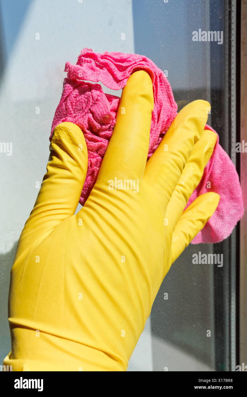 Parte in gomma gialla guanto lavaggio vetro della finestra mediante un panno umido Foto Stock