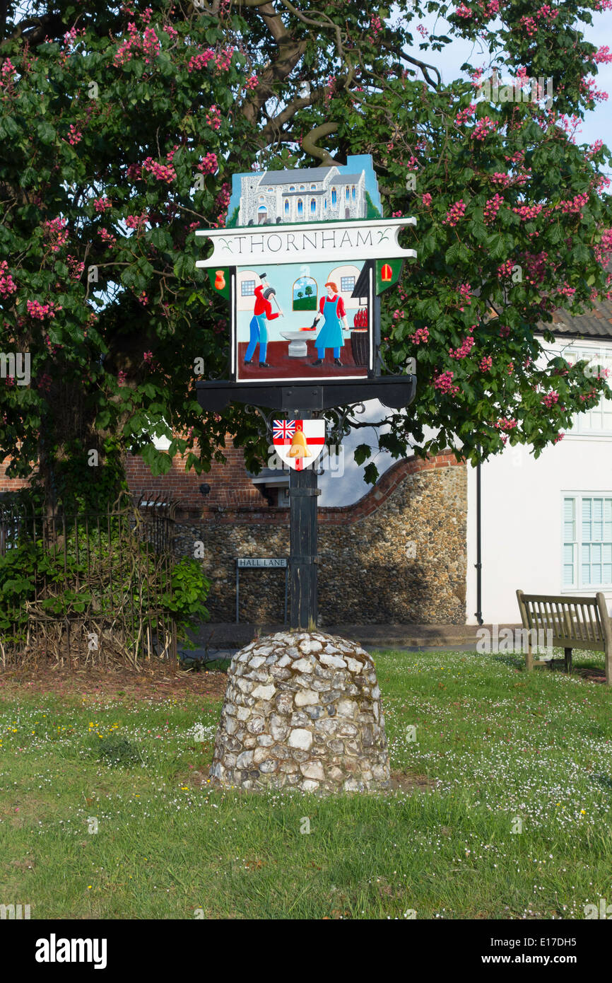 Villaggio verniciato segno per Thornham raffigurante la chiesa e i fabbri shop, di fronte ad una fioritura castagno Foto Stock