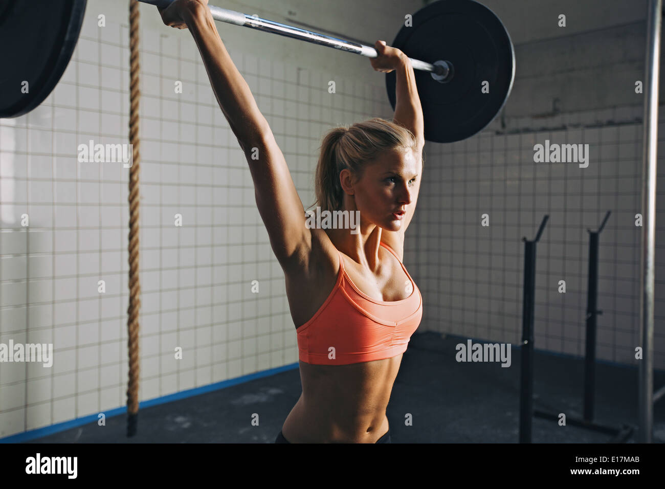 Donna forte sollevamento barbell come una parte di crossfit esercizio di routine. Montare la giovane donna di sollevamento pesi pesanti in palestra. Foto Stock