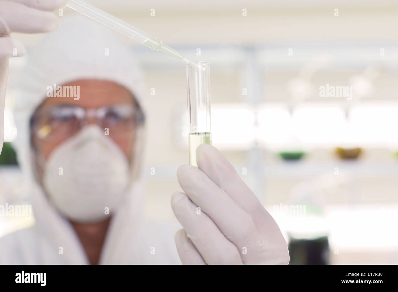 Scienziato in clean suit utilizzando una pipetta e provetta di test in laboratorio Foto Stock