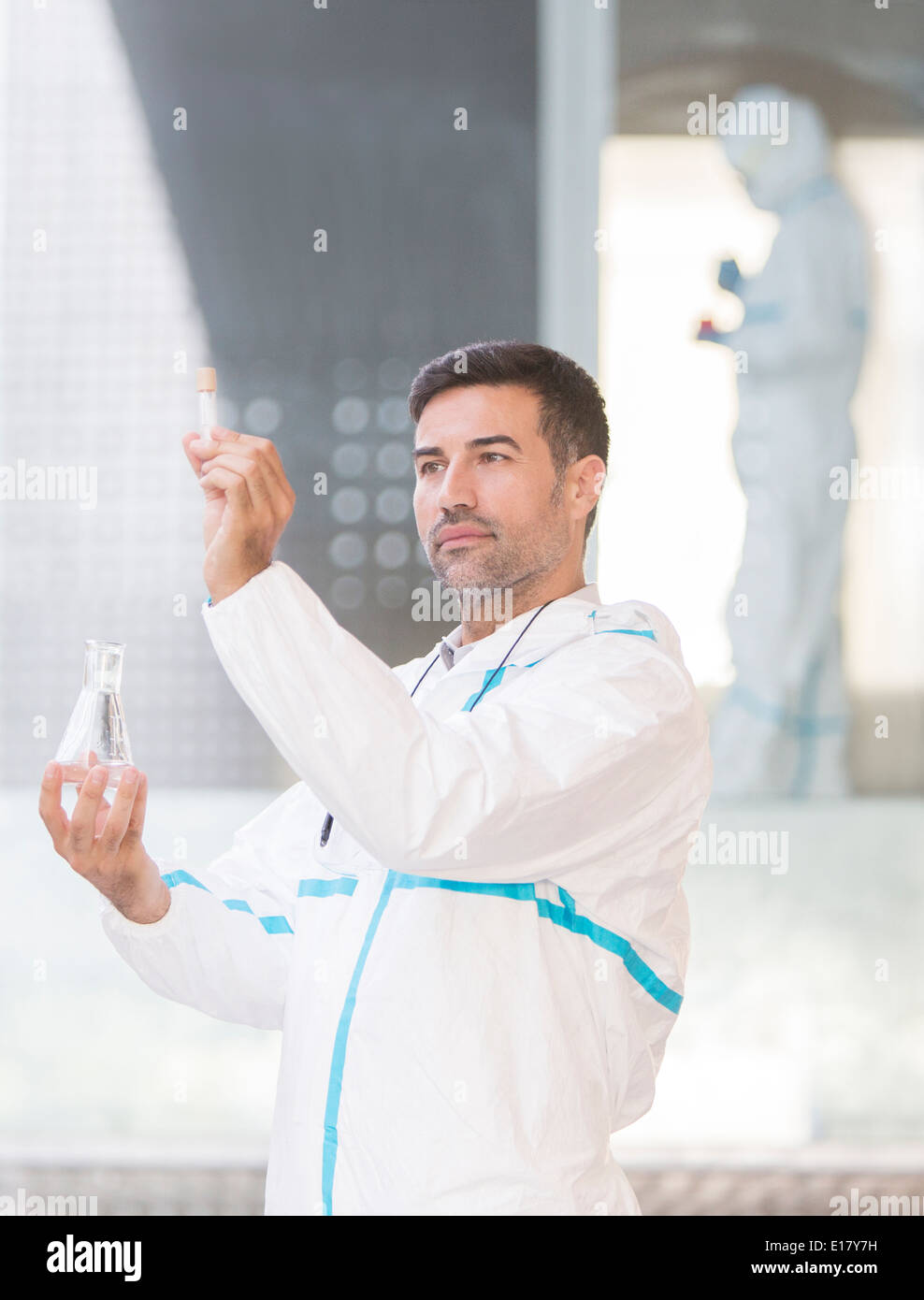 Scienziato in clean suit esaminando il liquido nel tubo di prova Foto Stock