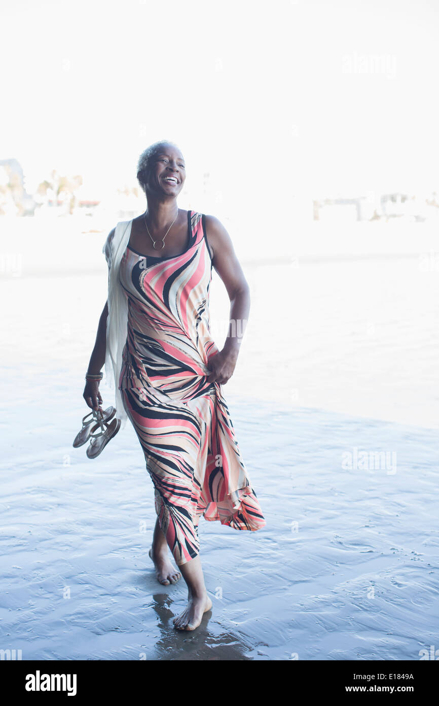 Donna felice nel vestire correre a piedi nudi sulla spiaggia Foto Stock