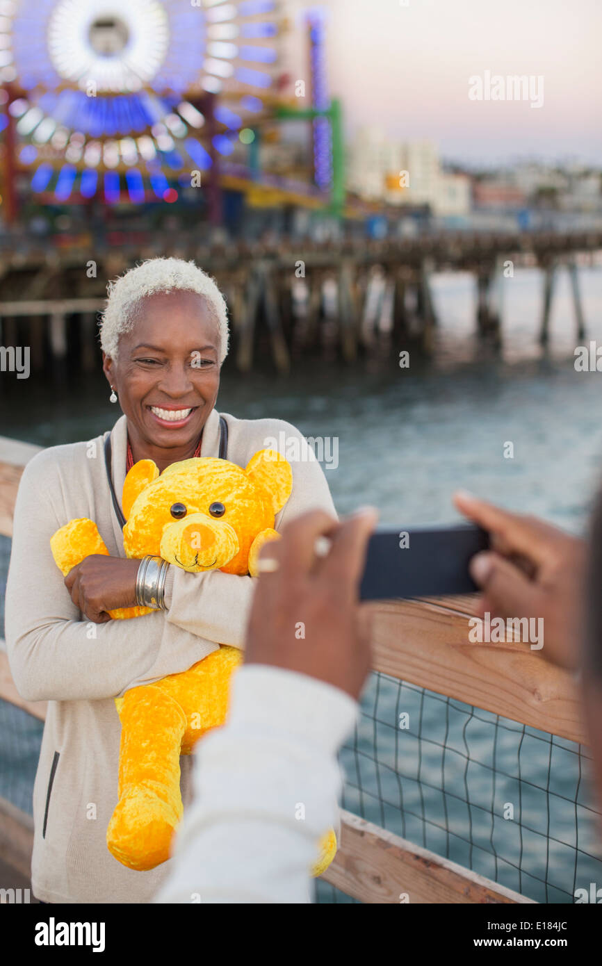 Senior donna con orsacchiotto che posano per una fotografia al parco divertimenti Foto Stock