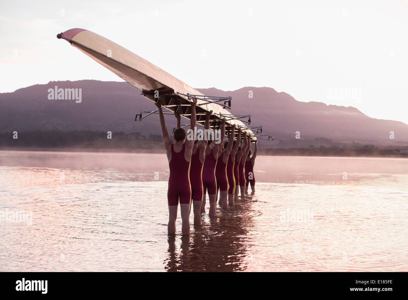 Il team di canottaggio che trasportano fila overhead in barca nel lago ancora Foto Stock