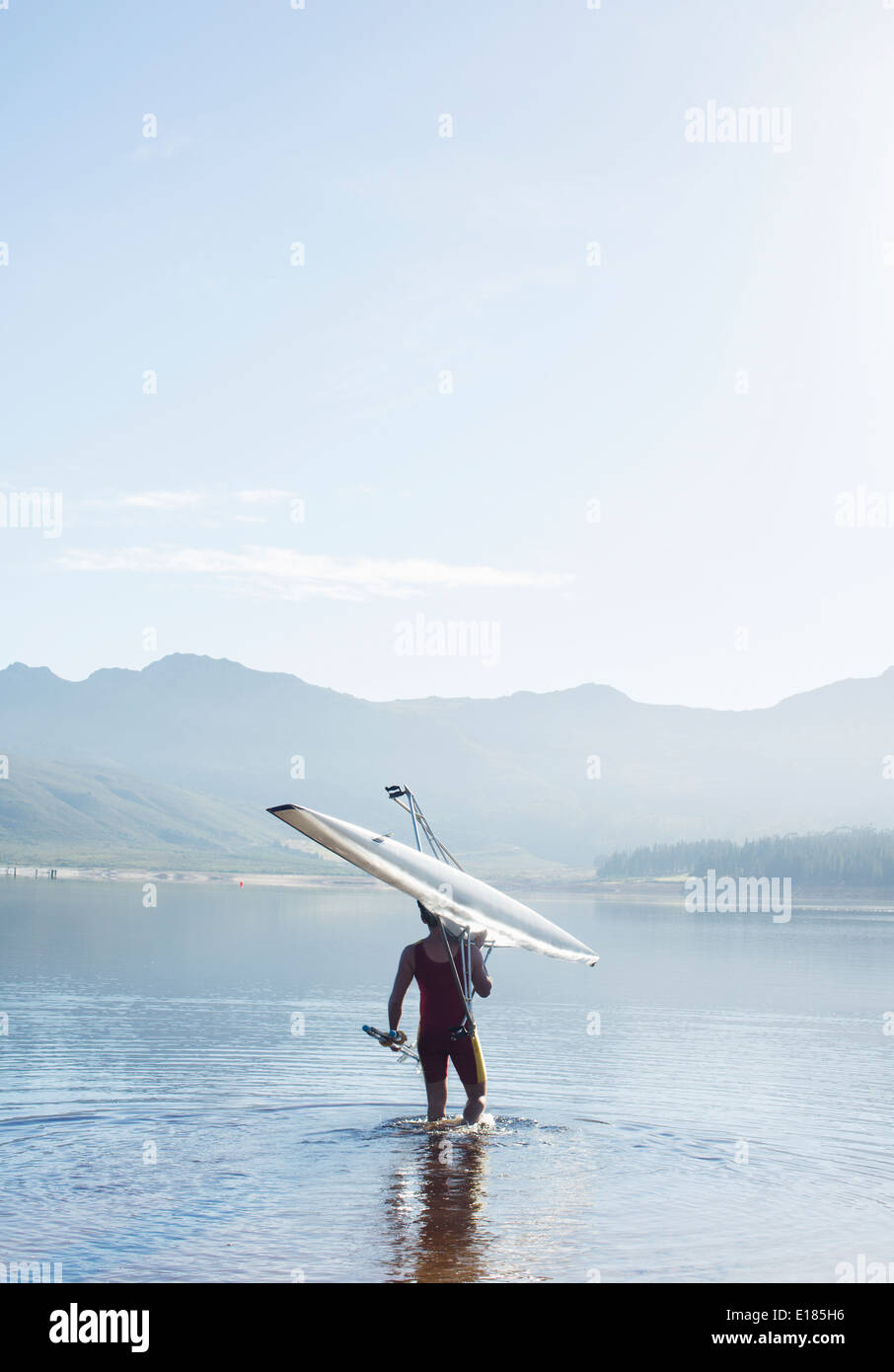 Uomo che porta il canottaggio scull nel lago Foto Stock