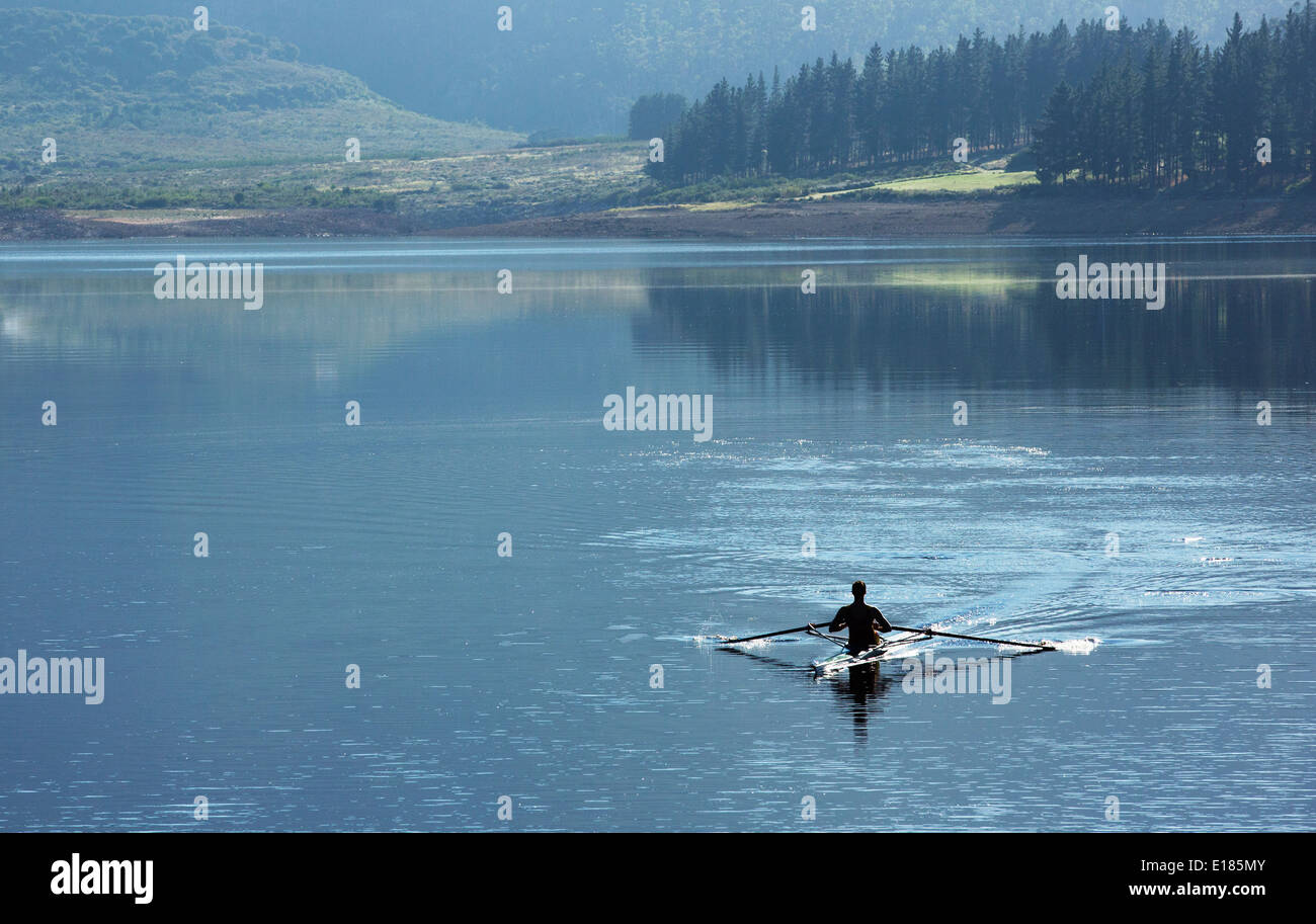Uomo scull canottaggio sul lago Foto Stock