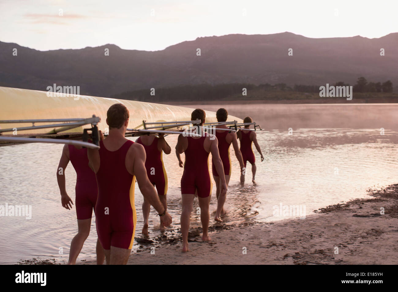 Il team di canottaggio che trasportano scull nel lago all'alba Foto Stock