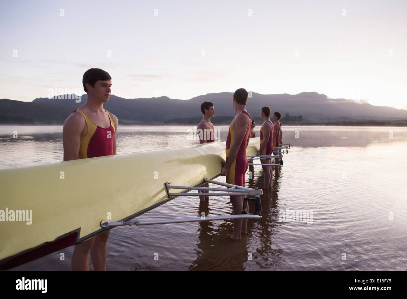Il team di canottaggio holding scull nel lago all'alba Foto Stock