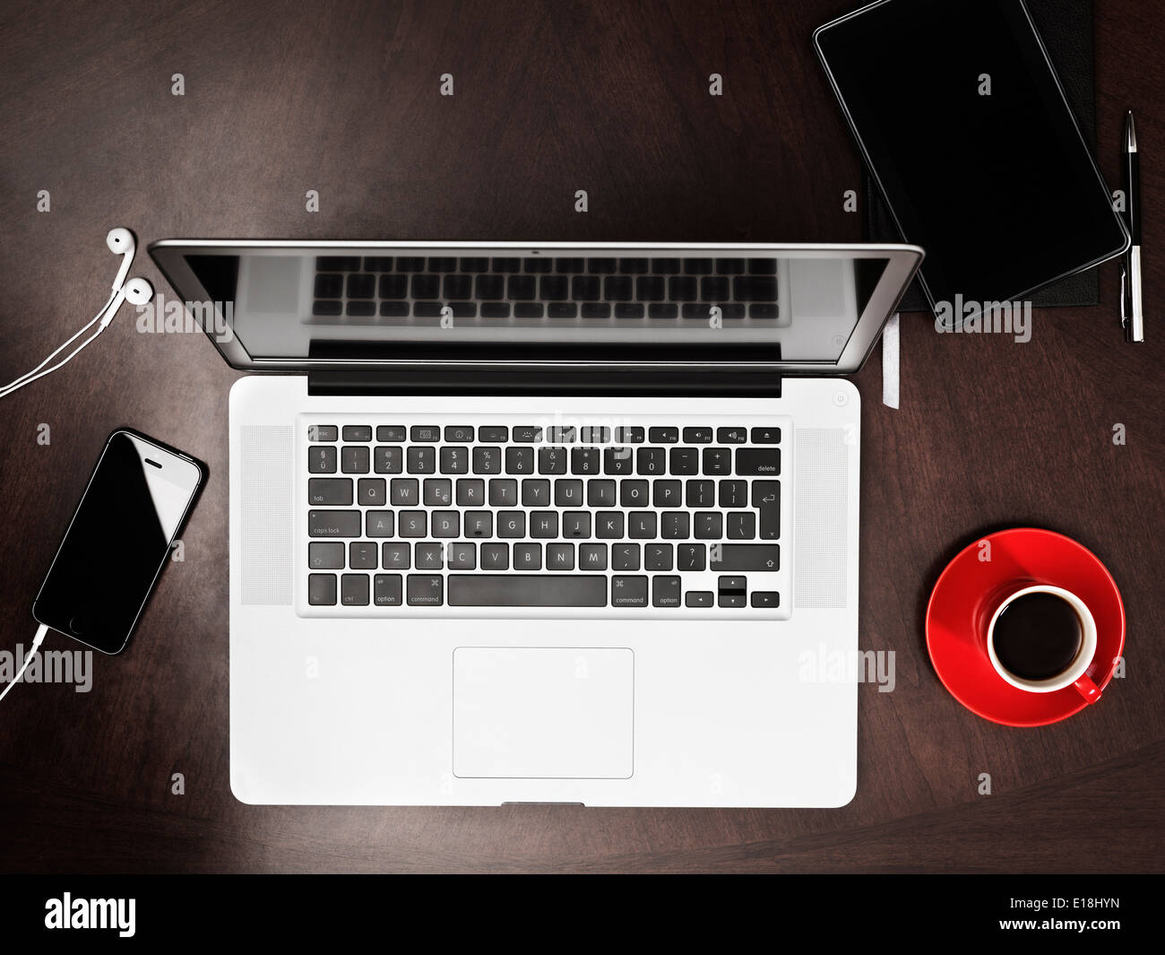 Macbook Apple computer portatile, iPhone Kindle tablet e una tazza di caffè sulla scrivania. Angolo di Alta Vista. Foto Stock